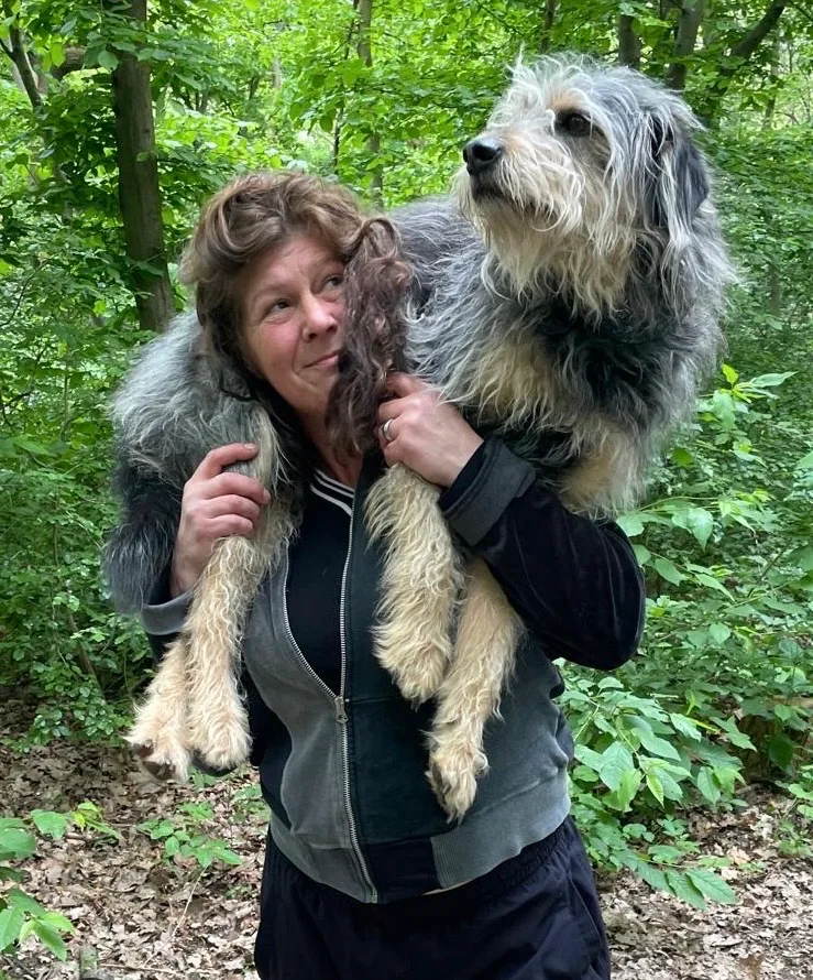 Manuela Zimmermann trägt ihren zotteligen Hund auf den Schultern durch den Wald und lächelt ihn an